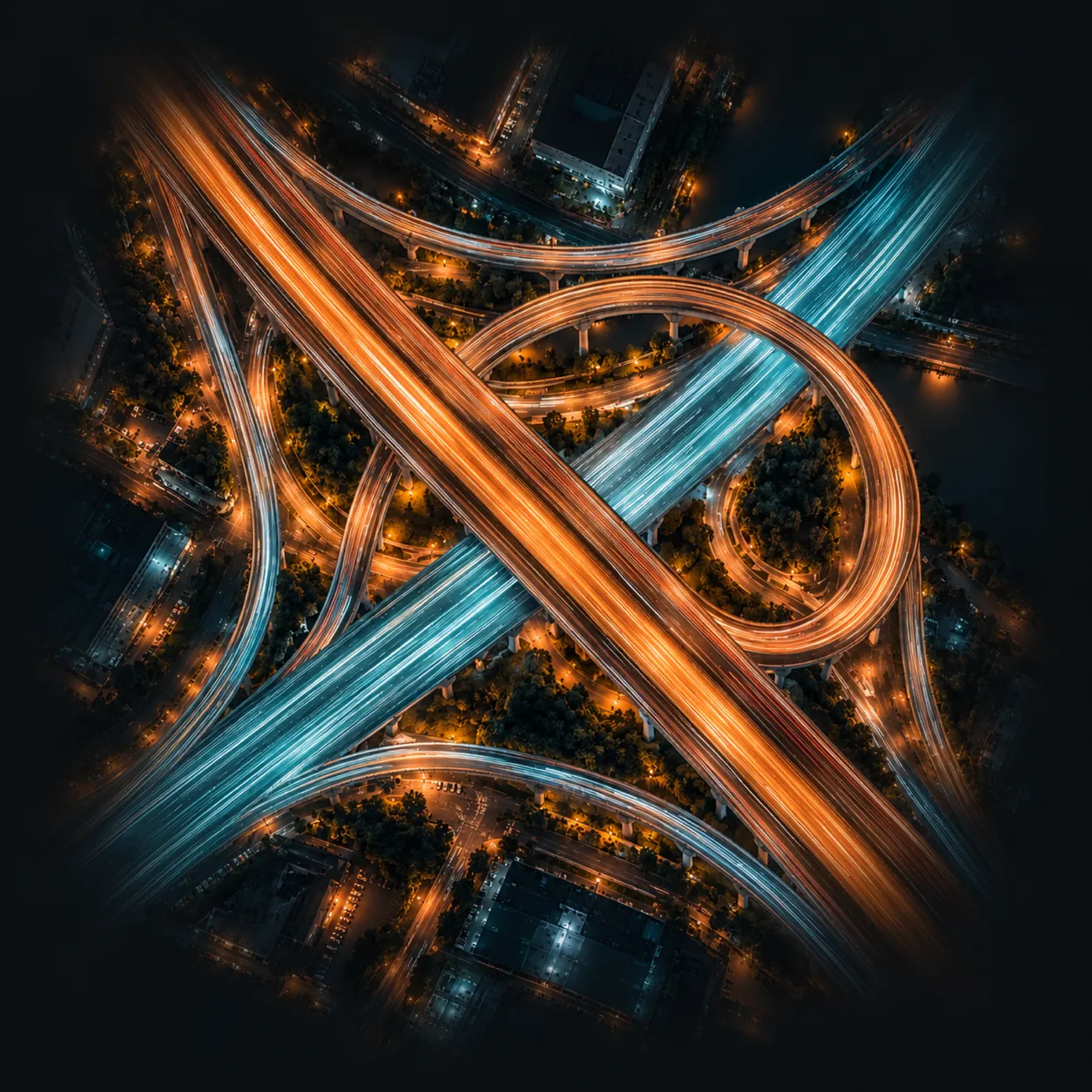 Aerial night view of an elevated highway interchange, with amber and aqua light trails looping through it.